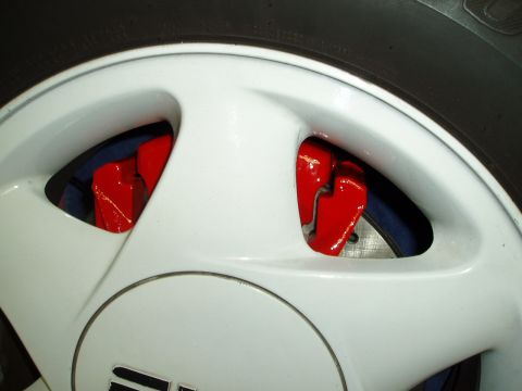 1993 Ford Taurus - Close-up view of red brake calipers peeking through the spokes of a white wheel.