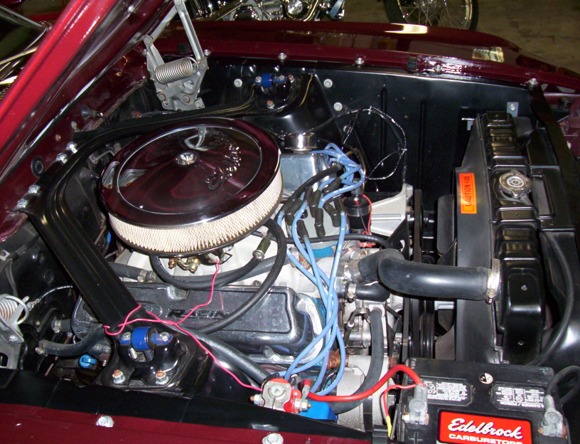 Maroon Mustang engine bay with chrome air cleaner, blue plug wires, and Edelbrock battery decal