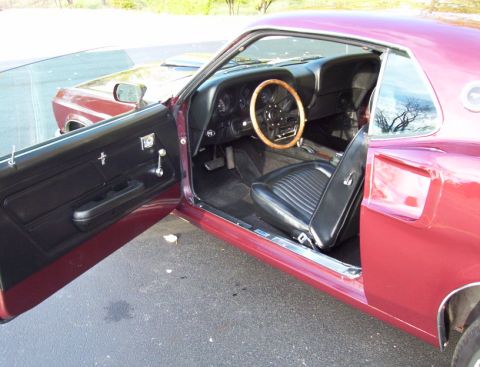 1969 Ford Mustang - The interior of a 1969 Ford Mustang shows black vinyl seats and a wooden steering wheel.
