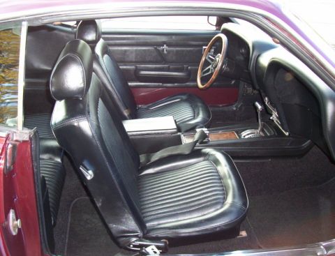 1969 Ford Mustang - The interior of a classic car, black vinyl seats and a wooden steering wheel.