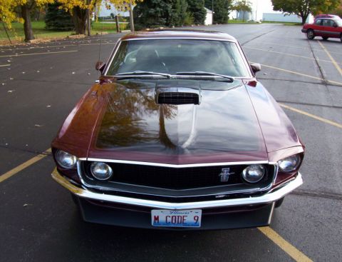 1969 Ford Mustang - A maroon 1969 Ford Mustang is parked in a lot with a red car in the background.