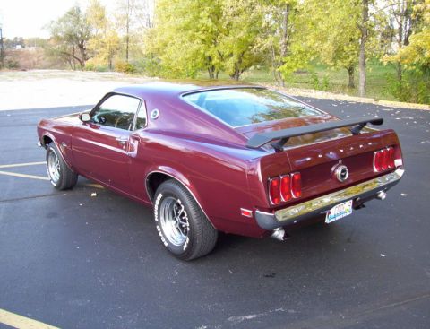 1969 Ford Mustang - A maroon 1969 Ford Mustang is parked on asphalt with trees in the background.