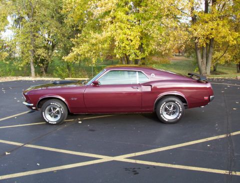 1969 Ford Mustang - This maroon 1969 Ford Mustang fastback features a distinctive body style and a rear spoiler, captured in a side profile view.