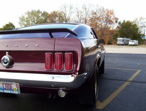 1969 Ford Mustang - The rear of a classic Mustang is shown parked in a lot with trees in the background.