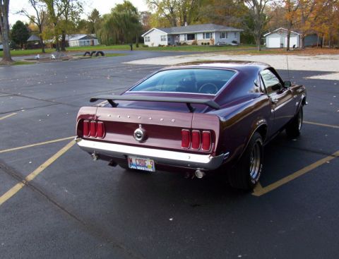 1969 Ford Mustang - A maroon 1969 Ford Mustang is parked in a lot, showing its distinctive rear end and spoiler.
