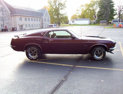 1969 Ford Mustang - This 1969 Ford Mustang fastback is shown in a side profile, parked in a lot with a building in the background.