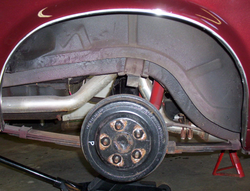 Underside rear suspension and brake drum of a maroon vehicle on a lift