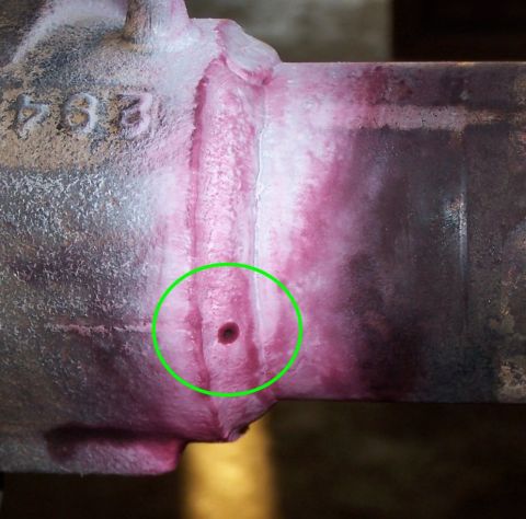 1979 Ford Bronco - Extreme close-up of a cast-metal component with a bead weld running vertically across it, coated in pink dye-penetrant inspection fluid; a…