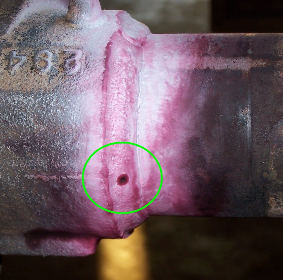 Weld on cast part with pink dye-penetrant and circled pinhole defect