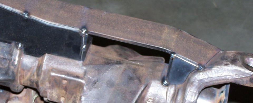 Close-up of rusty vehicle frame with welded metal brackets and drivetrain components