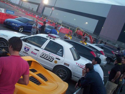 1998 Ford Crown Victoria - white Ford Crown Victoria with BBS, Tokico and Kenny Brown decals surrounded by spectators at a dusk motorsport event.