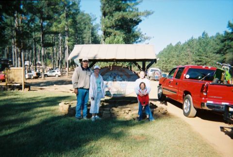 2003 Ford F-350 - A family poses in front of a sign at a campsite, with a red pickup truck loaded with ATVs parked nearby.