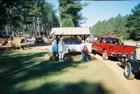 2003 Ford F-350 - A red SUV is parked on a dirt road, towing a trailer with ATVs, with people standing nearby.