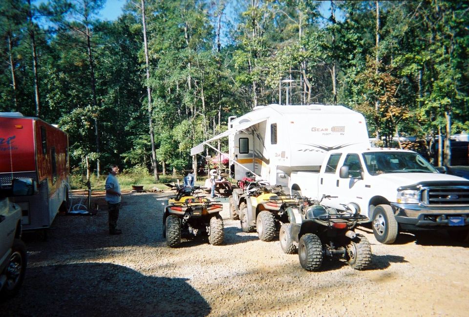 White Ford F-350 truck towing a camper, with several ATVs parked nearby