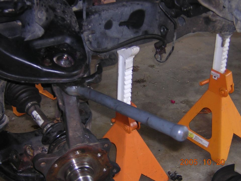Truck front suspension on orange jack stands with wheel removed, showing hub, CV axle and pry bar