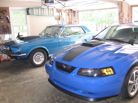 1967 Ford Mustang - Two Ford Mustangs, a classic 1967 coupe and a modern model, parked side-by-side in a garage.