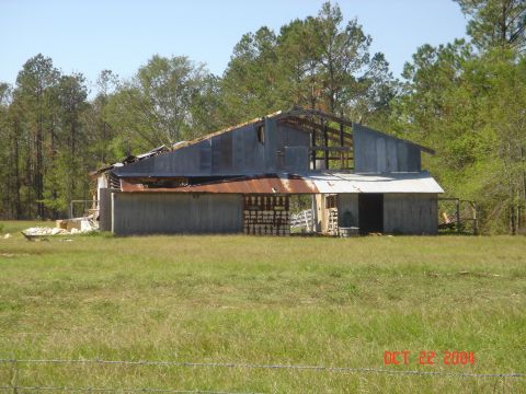 2002 Jeep Wrangler - This old barn shows significant damage to its roof and structure, with overgrown grass in the foreground.
