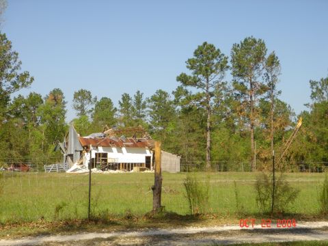 2002 Jeep Wrangler - A rural scene shows a barn with significant storm damage, its roof partially collapsed and debris scattered around.