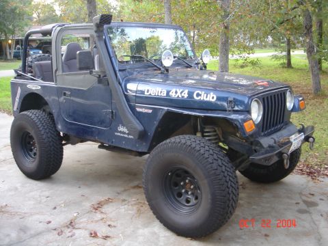 2002 Jeep Wrangler - A blue Jeep Wrangler is parked on a concrete driveway, modified for off-road use with a snorkel and large tires.