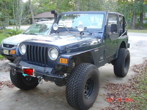 2002 Jeep Wrangler - A blue Jeep Wrangler is parked in a driveway, equipped with a snorkel and large off-road tires.
