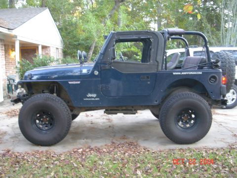 2002 Jeep Wrangler - Blue 2002 Jeep Wrangler parked in a driveway with trees and a house in the background.