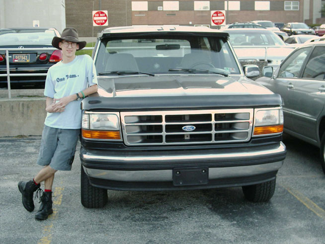 Person leaning on front of gray and black Ford SUV in parking lot