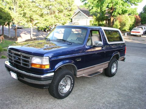 1996 Ford Bronco - This blue Ford Bronco is parked in a driveway with trees and houses in the background.