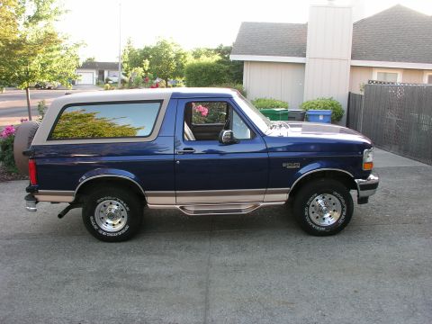 1996 Ford Bronco - A blue 1996 Ford Bronco is parked on a concrete driveway in front of a house.
