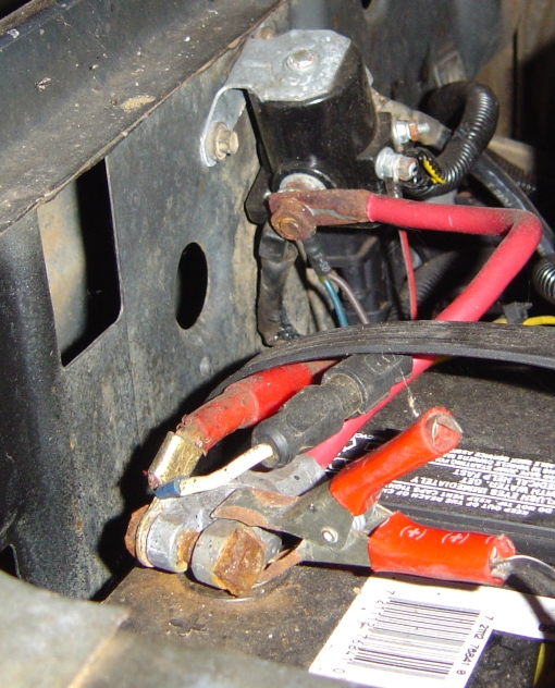 Corroded starter solenoid on inner fender with red battery cables and heat-shrink terminals