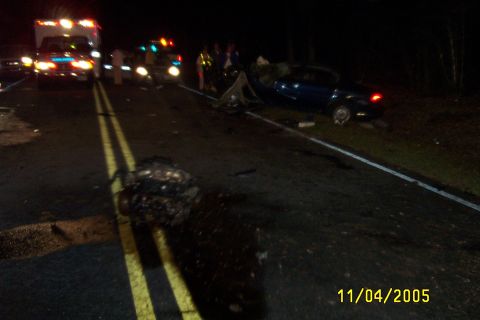 1998 Ford Crown Victoria - A nighttime scene of a car wreck with emergency vehicles present and debris scattered on the road.