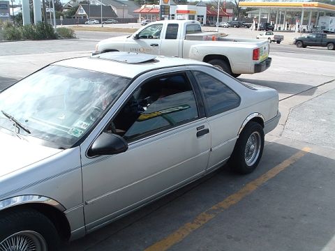1992 Ford Thunderbird - A silver 1992 Ford Thunderbird coupe is seen from the side at a gas station, with a white pickup truck in the background.