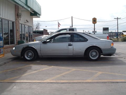 1992 Ford Thunderbird - Side view of a silver 1992 Ford Thunderbird parked in a lot next to a building.