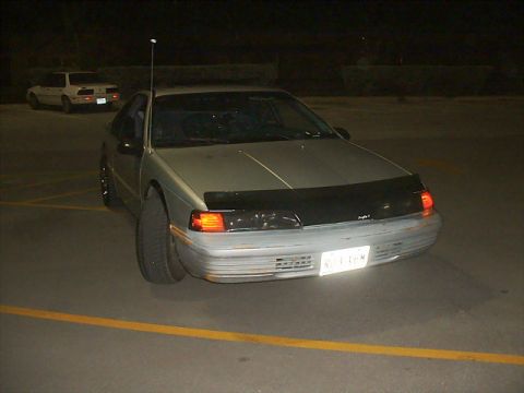1992 Ford Thunderbird - A silver 1992 Ford Thunderbird coupe is parked at night, showing its front end with a black bug deflector and a license plate.
