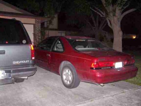 1994 Ford Thunderbird - A red 1994 Ford Thunderbird coupe is parked next to a Chevrolet SUV in a driveway at night.