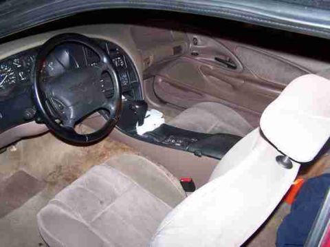 1994 Ford Thunderbird - The interior of a 1994 Ford Thunderbird features a tan cloth interior with a prominent dashboard and steering wheel.
