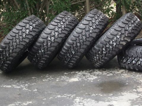 1996 Ford Bronco - Four off-road tires are displayed on a concrete surface with greenery in the background.