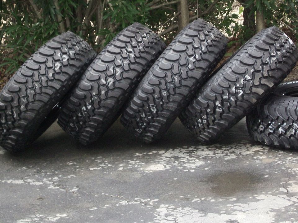 Four off-road tires with aggressive tread patterns leaning against each other on a concrete surface