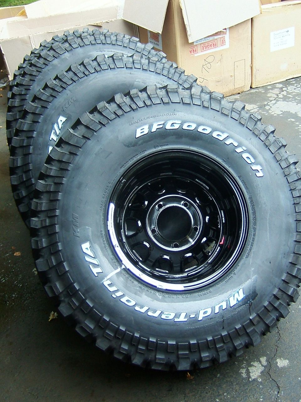 Three BFGoodrich Mud-Terrain T/A tires mounted on black steel rims, stacked in a row