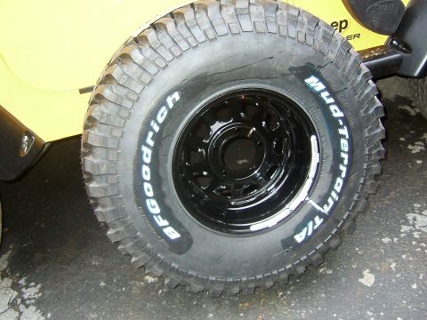1996 Ford Bronco - A BFGoodrich Mud-Terrain T/A tire is mounted on a black rim, with the yellow body of a vehicle in the background.