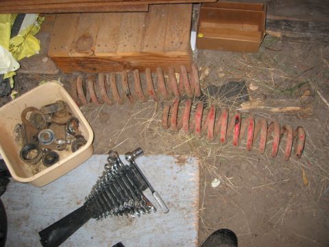 1991 Ford Explorer - Two long red-marked coil springs laid out on a dirt shop floor during a suspension teardown, next to a plastic tub of removed bushings, spa…