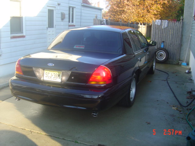 Dark Ford Crown Victoria parked in driveway, rear view. License plate SCJ-38M