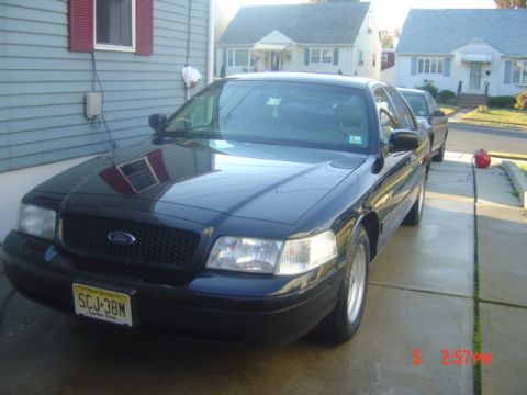 1999 Ford Crown Victoria - A black Ford Crown Victoria is parked in a driveway, with another vehicle visible behind it.