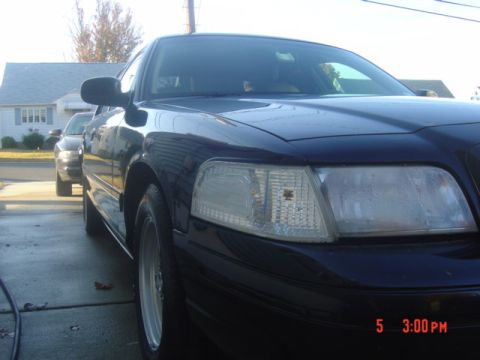 1999 Ford Crown Victoria - A dark sedan is parked in a driveway, with another vehicle visible in the background.