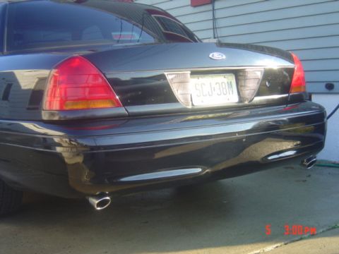 1999 Ford Crown Victoria - The rear view of a black sedan, likely a 1998 model, shows its dual exhaust pipes and a license plate.