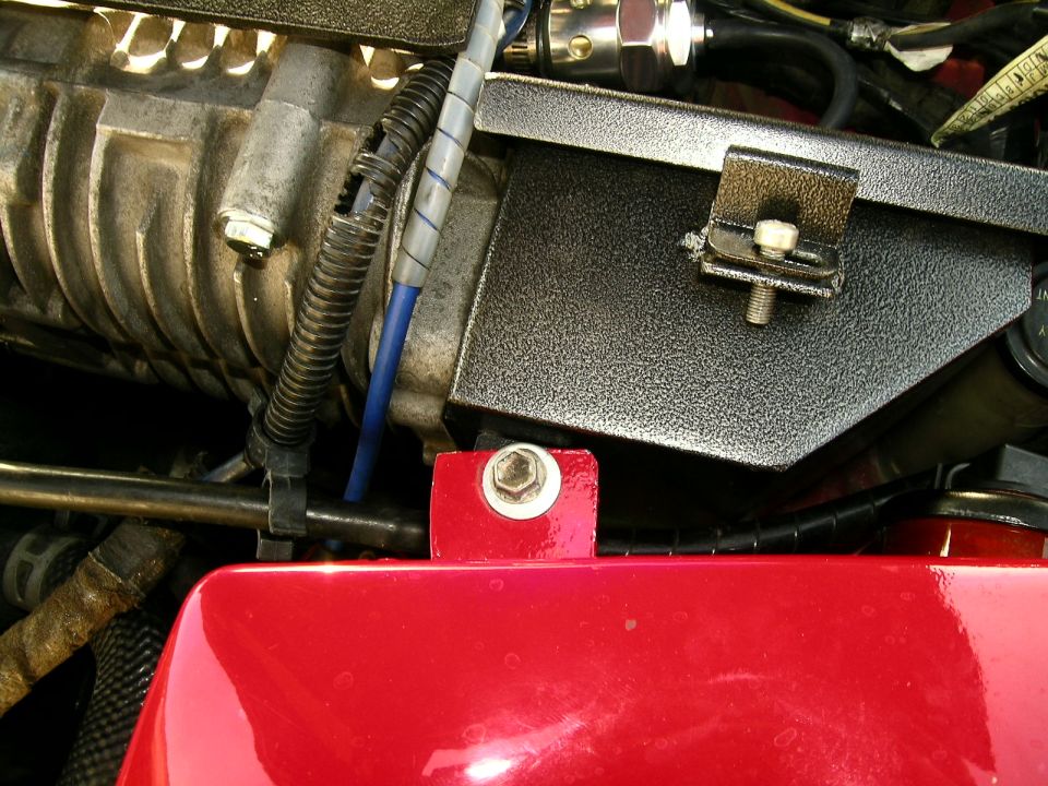 Engine bay close-up with black bracket, red bracket, bolts and blue wiring