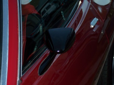 1972 Ford Ranchero - Close-up view of a red car's side door, a black side mirror and a chrome door handle. The reflection in the window shows another vehicle.