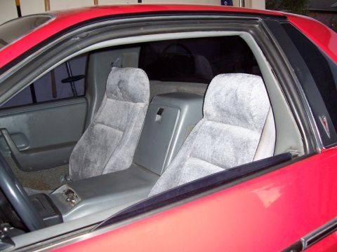 1988 Pontiac Fiero - The interior of a red car shows two gray bucket seats separated by a center console with storage.
