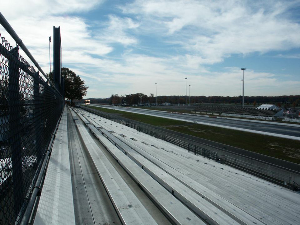 Aluminum bleachers overlook a drag strip under a cloudy sky