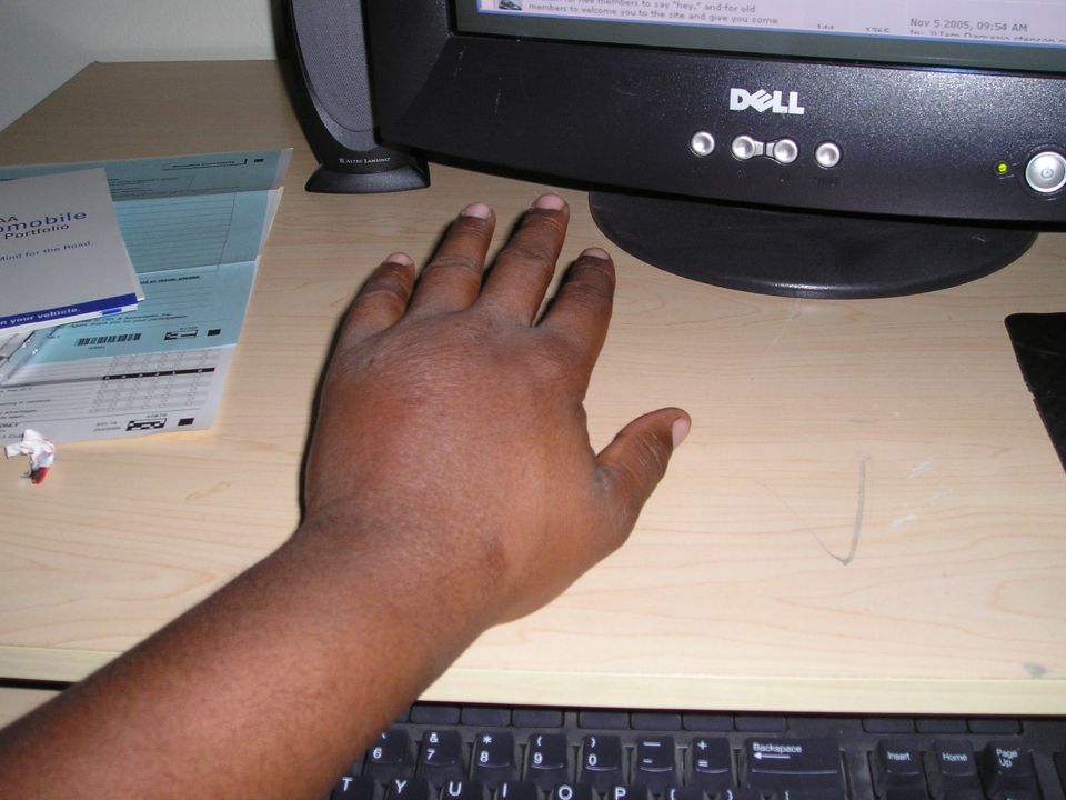 Hand resting on a wooden desk next to a Dell computer monitor and keyboard