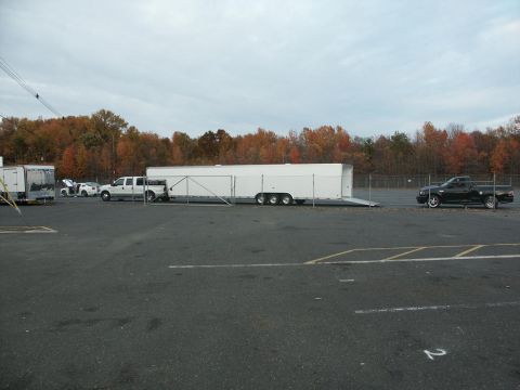 2001 Mercury Grand Marquis - A black pickup truck is seen towing a long white trailer in a parking lot with autumn trees in the background.